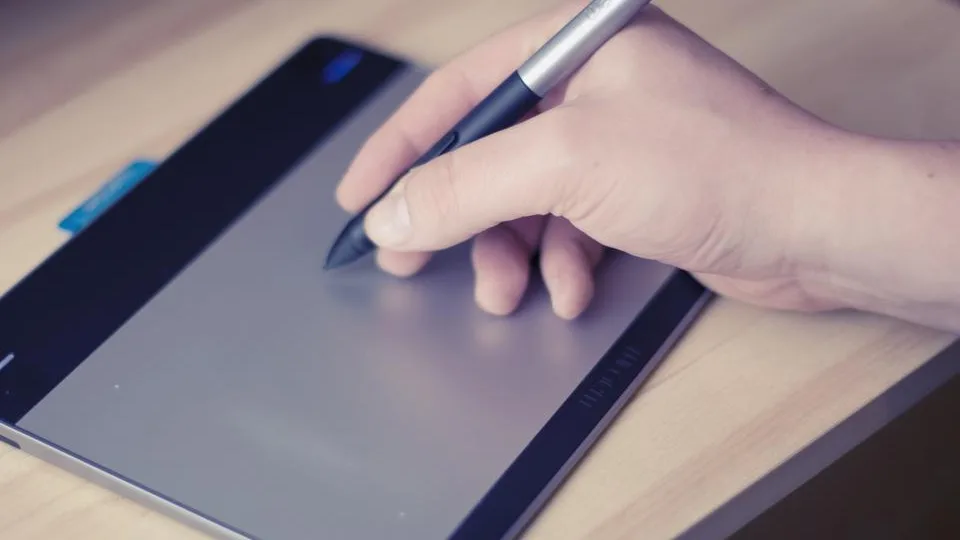Mão desenhando com caneta numa mesa digitalizadora sobre a mesa de trabalho