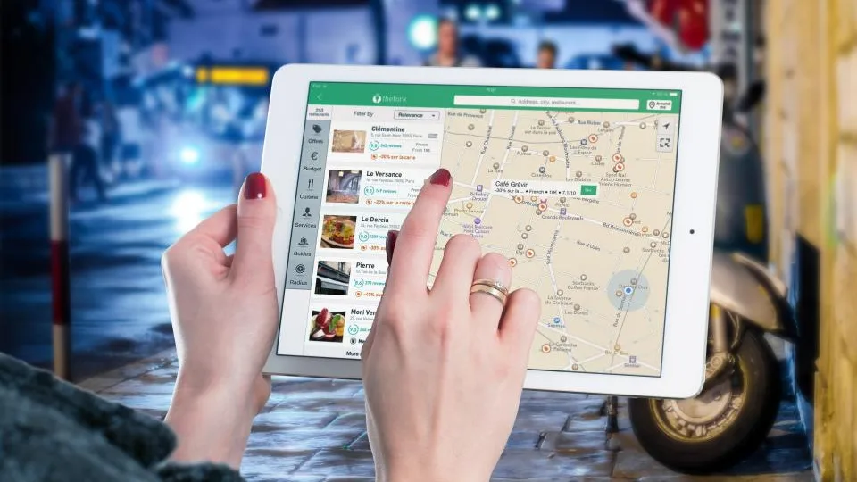 Mãos segurando um tablet com um mapa aberto na tela, ao ar livre